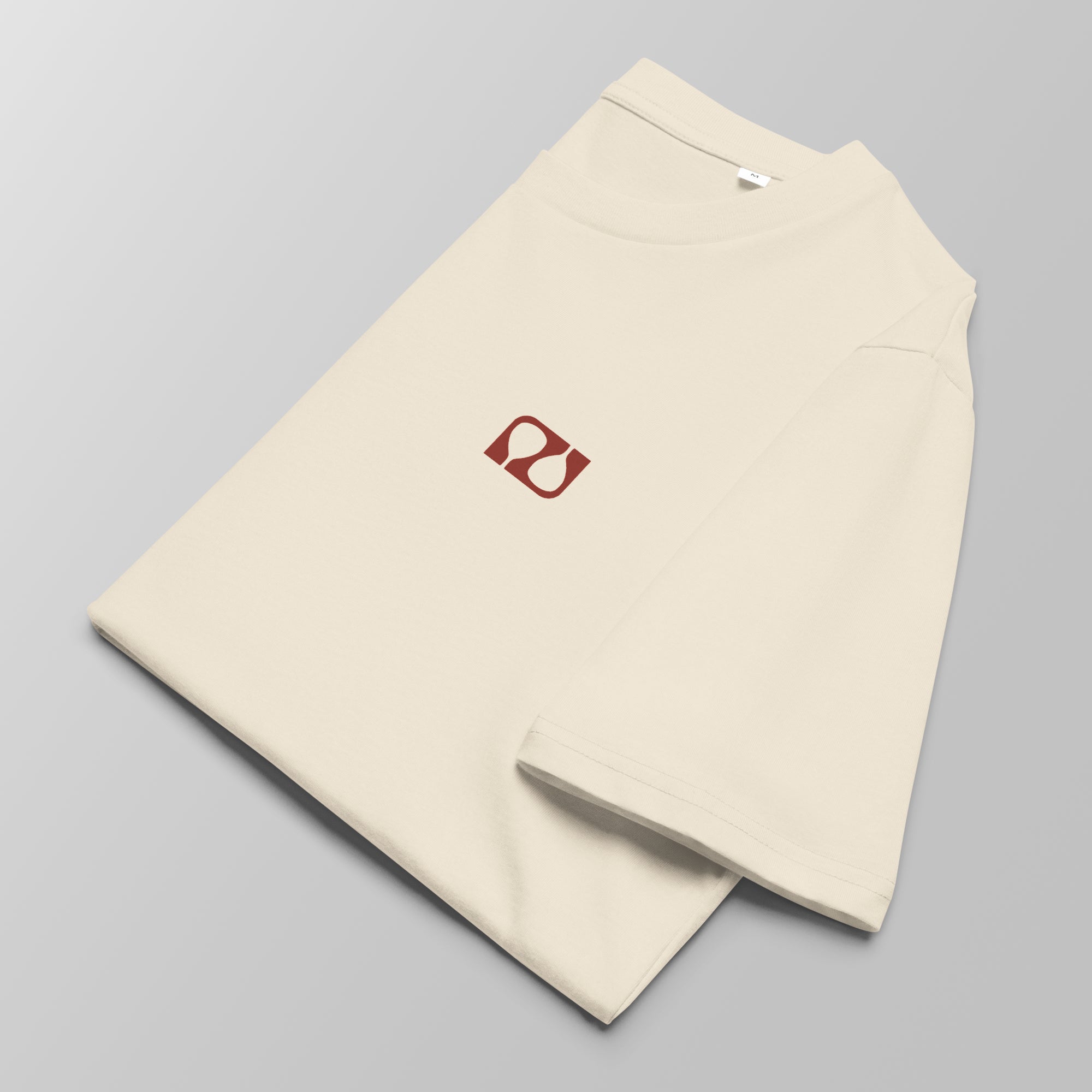 Close-up of a folded cream padel t-shirt with a small red logo on the left chest.