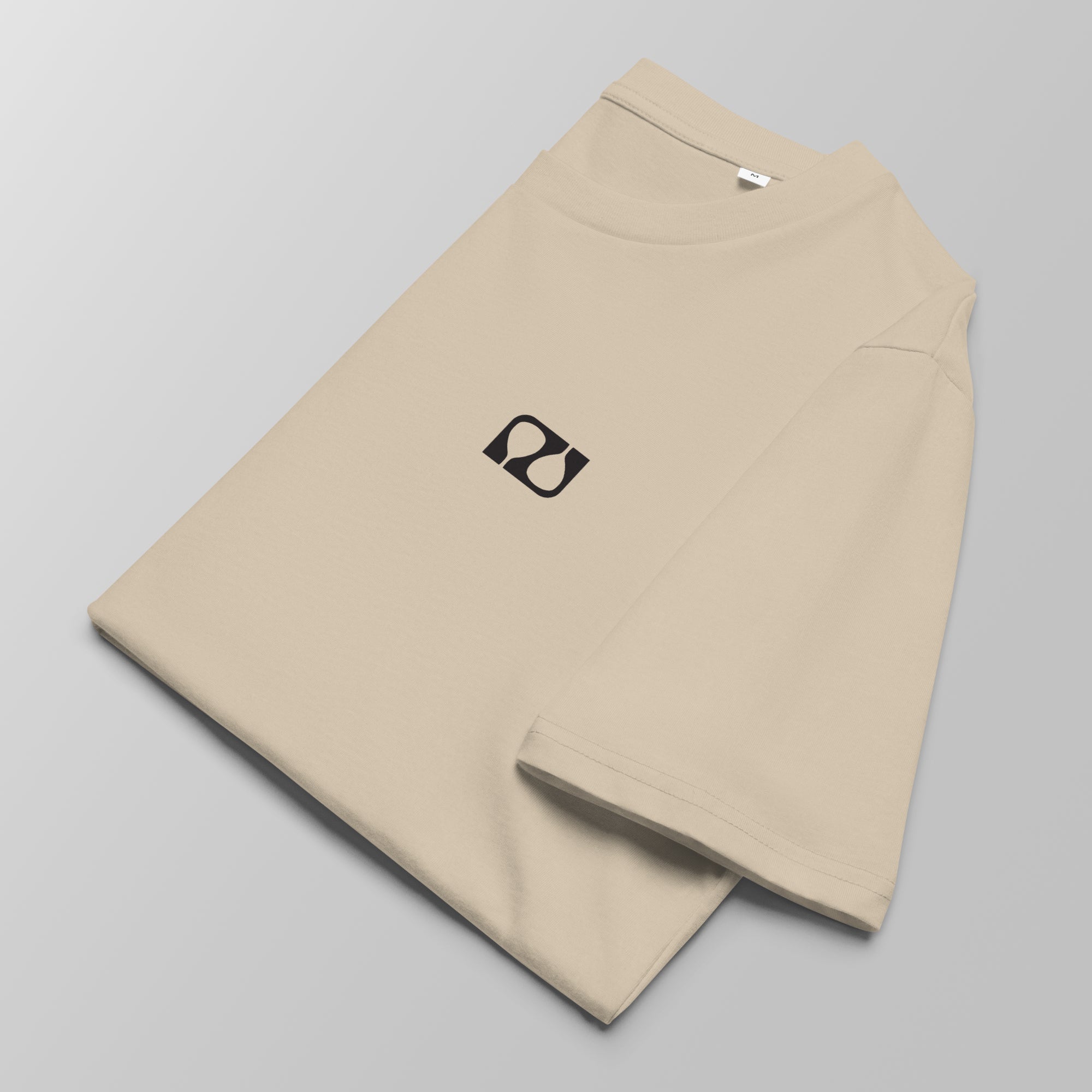 Close-up of a folded ecru padel t-shirt with a small black logo on the left chest.
