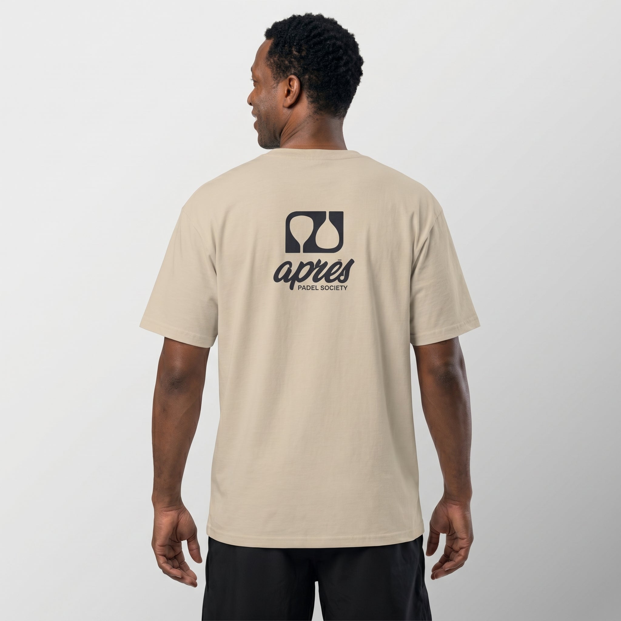Male model with back toward camera wearing an oversized ecru unisex padel t-shirt in relaxed fit with a black logo central on the back.