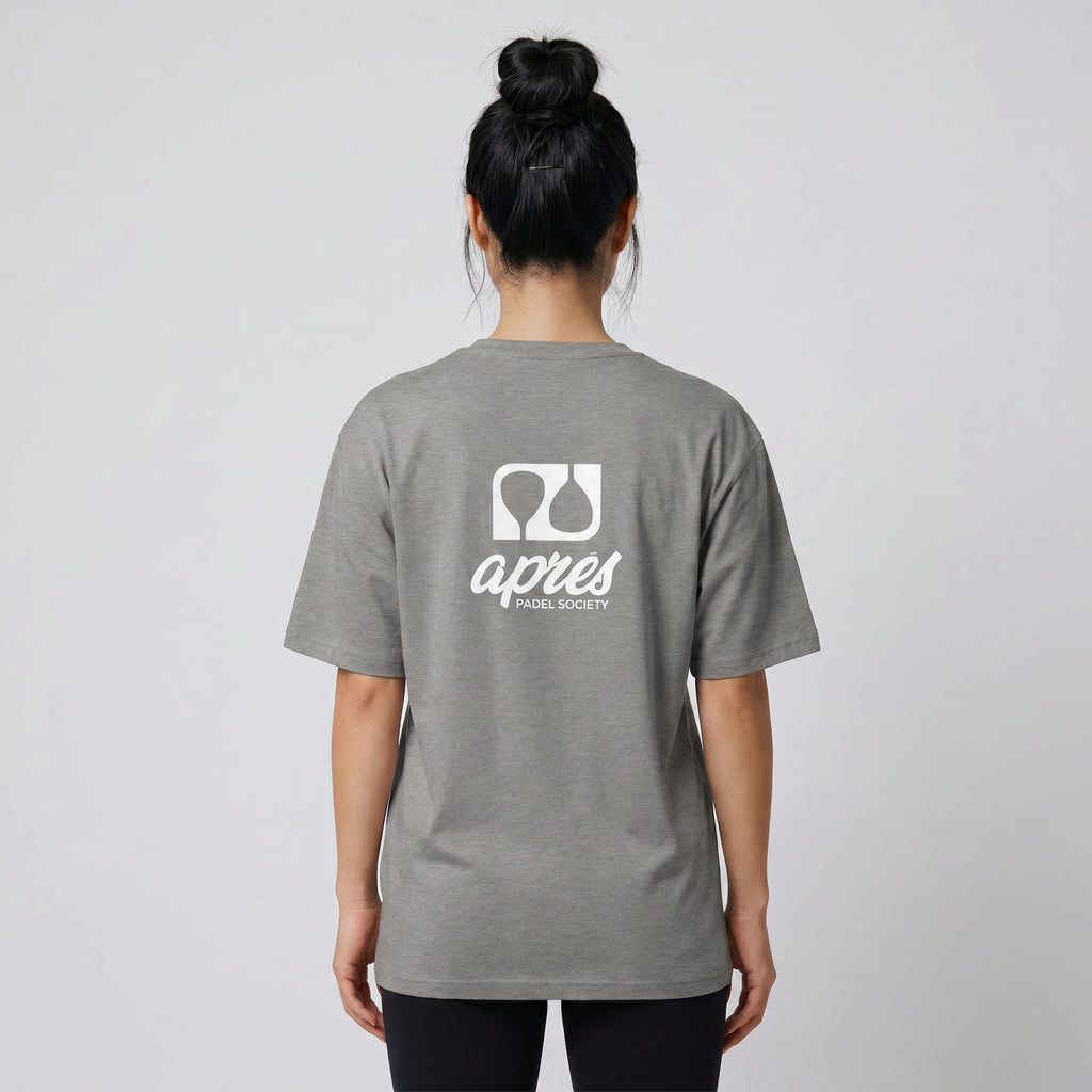 Female model with back toward camera wearing an oversized heather grey unisex padel t-shirt in relaxed fit with a white logo central on the back.
