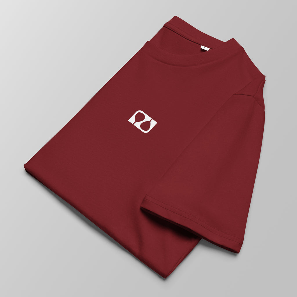 Close-up of a folded maroon padel t-shirt with a small white logo on the left chest.