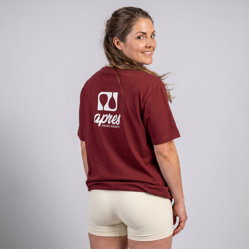 Female model with back toward camera wearing an oversized maroon unisex padel t-shirt in relaxed fit with a white logo central on the back.