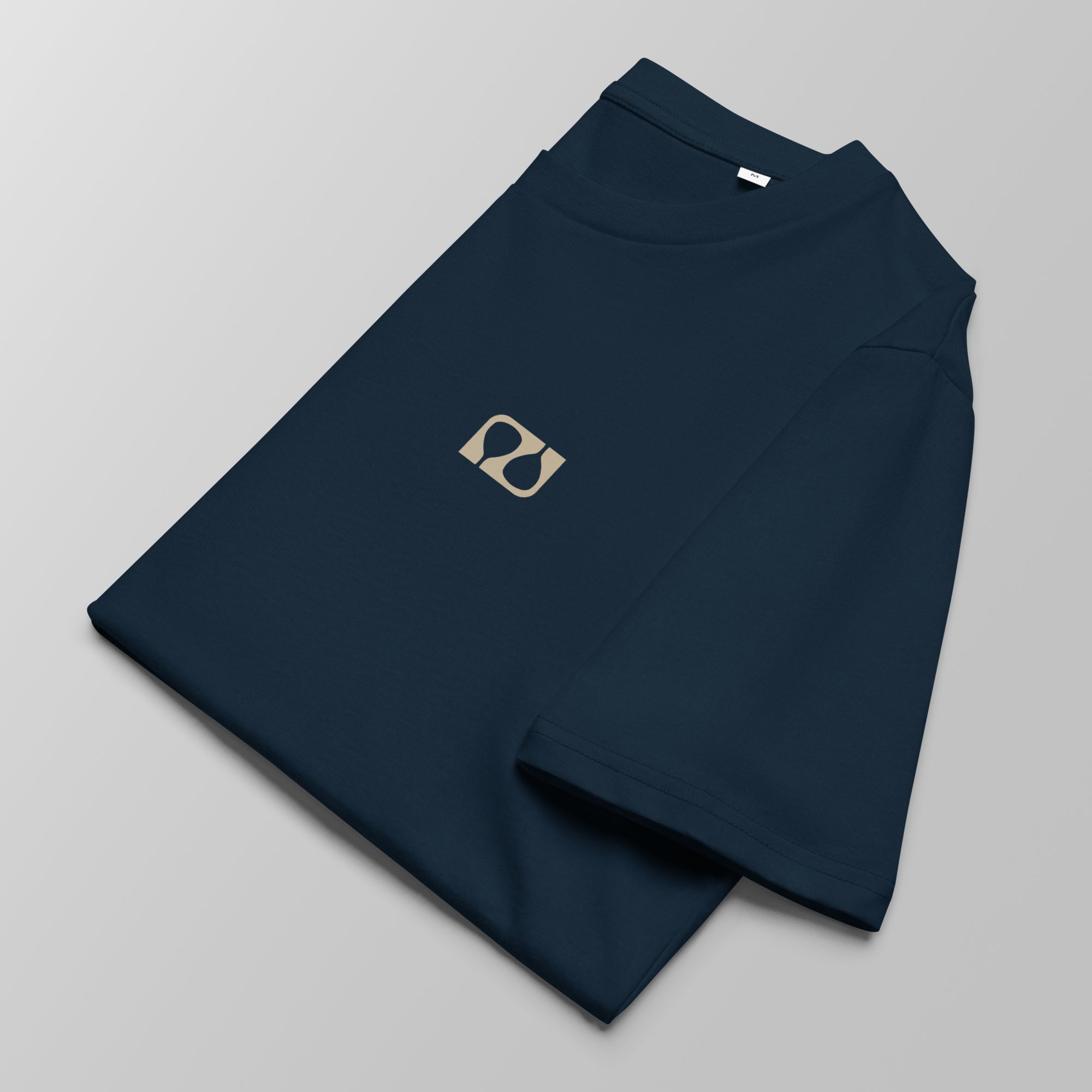 Close-up of a folded navy blue padel t-shirt with a small tan logo on the left chest.