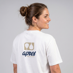 Female model with back toward camera wearing an oversized unisex white padel t-shirt in relaxed fit with a tan and navy logo central on the back.