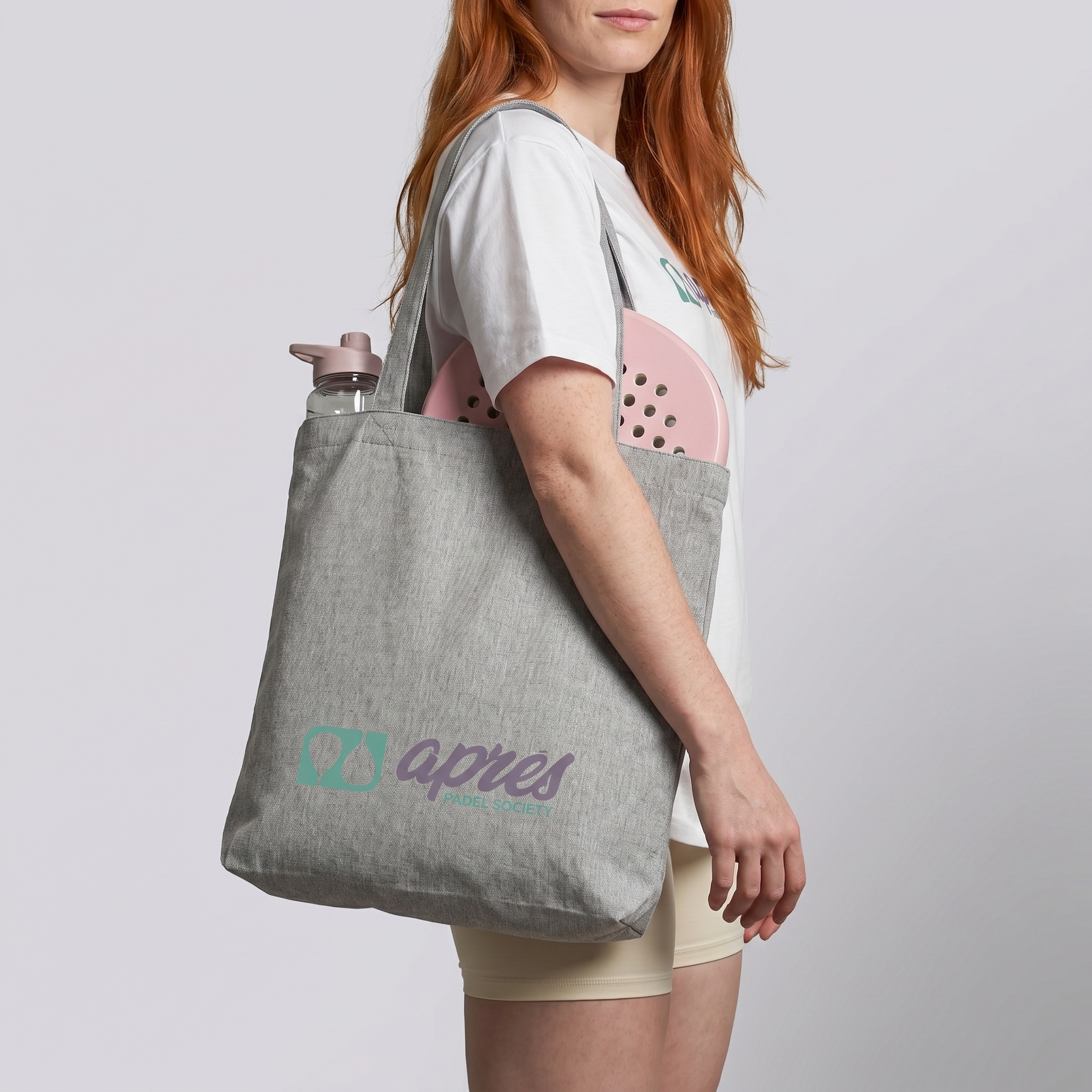 Model carrying a premium heather grey padel tote bag with visible padel racket and water bottle inside, featuring a green & purple 'Après Padel Society' logo.