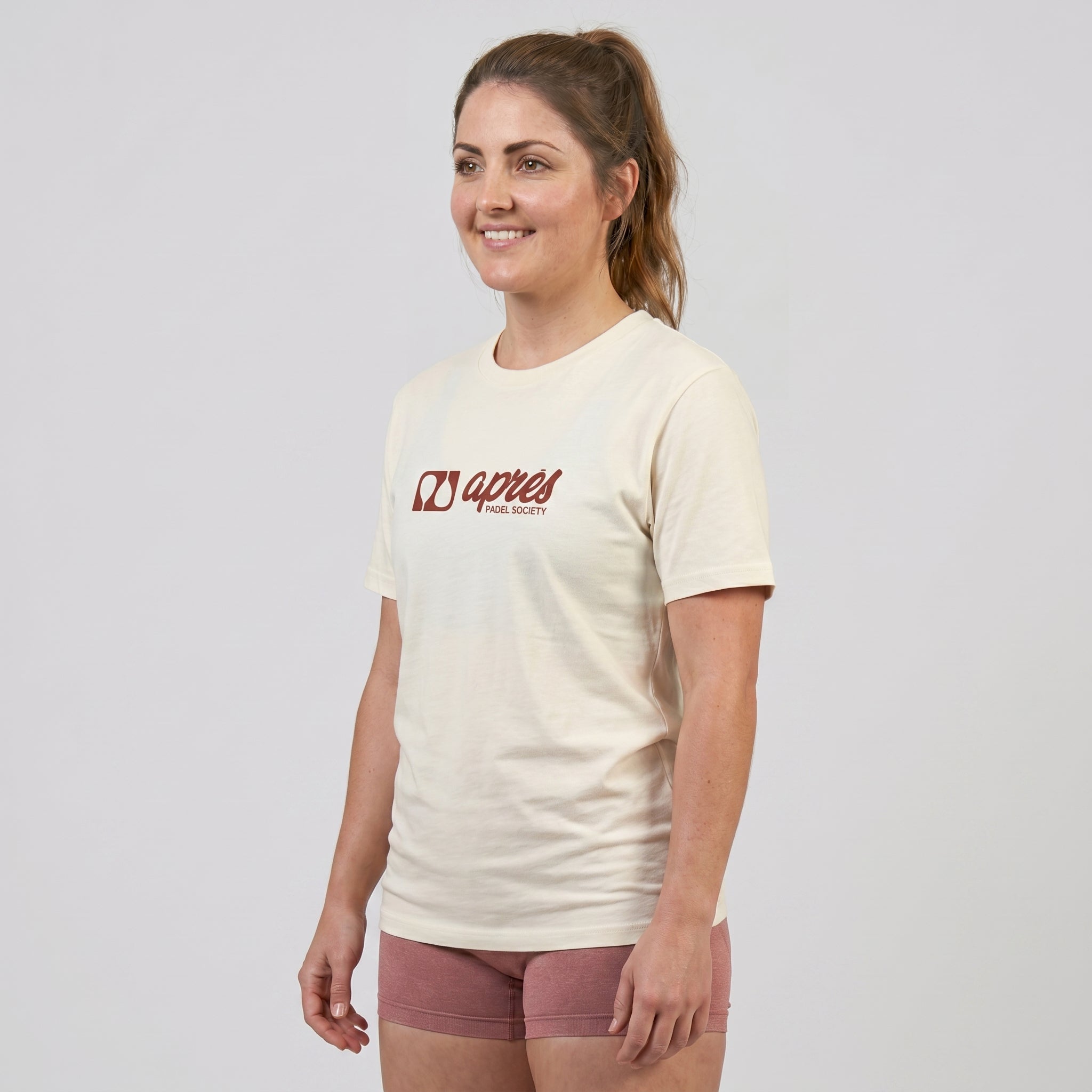 Female model wearing an oversized unisex cream padel t-shirt in relaxed fit with a red horizontal chest logo.