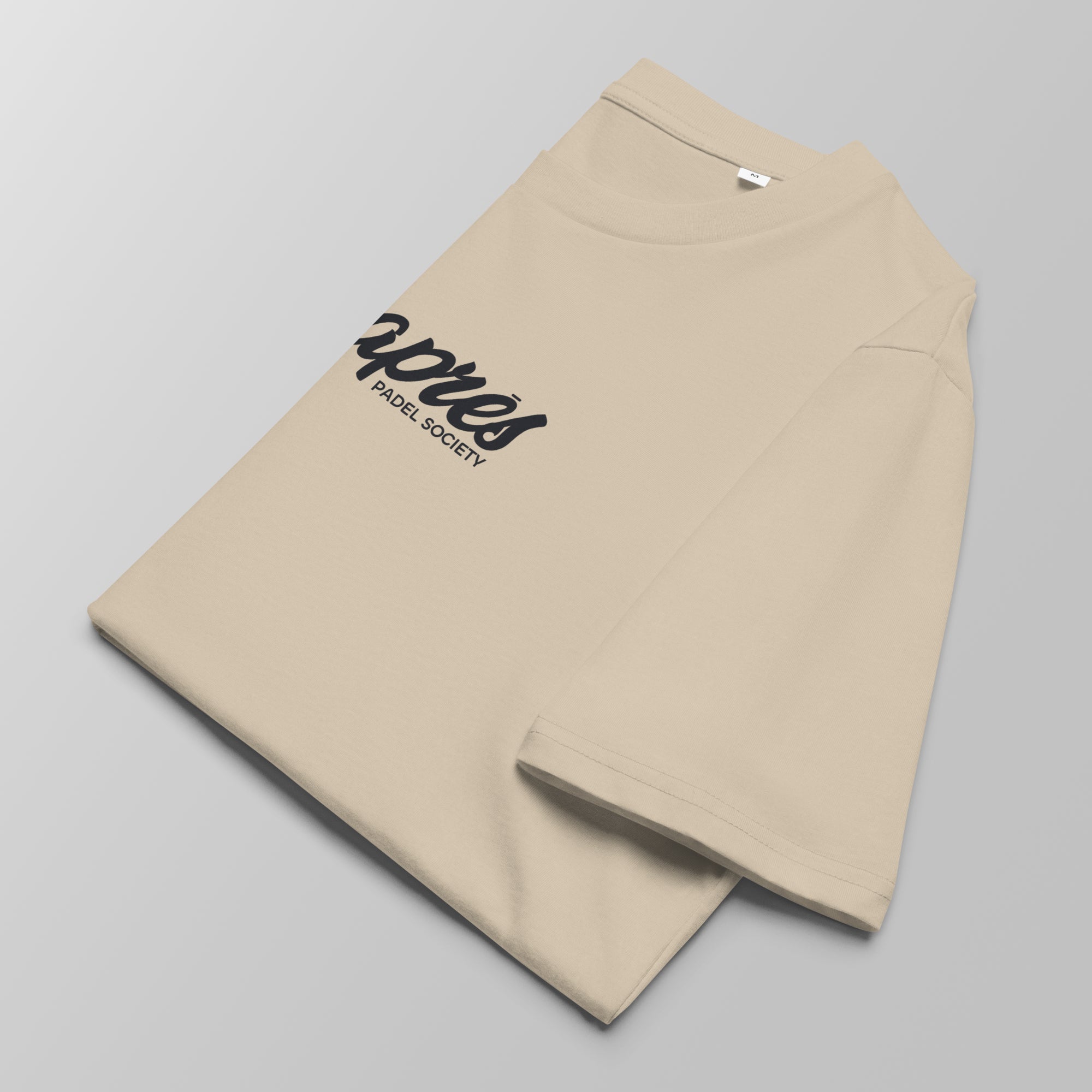 Close-up of a folded ecru padel t-shirt with black 'Après Padel Society' logo centred.