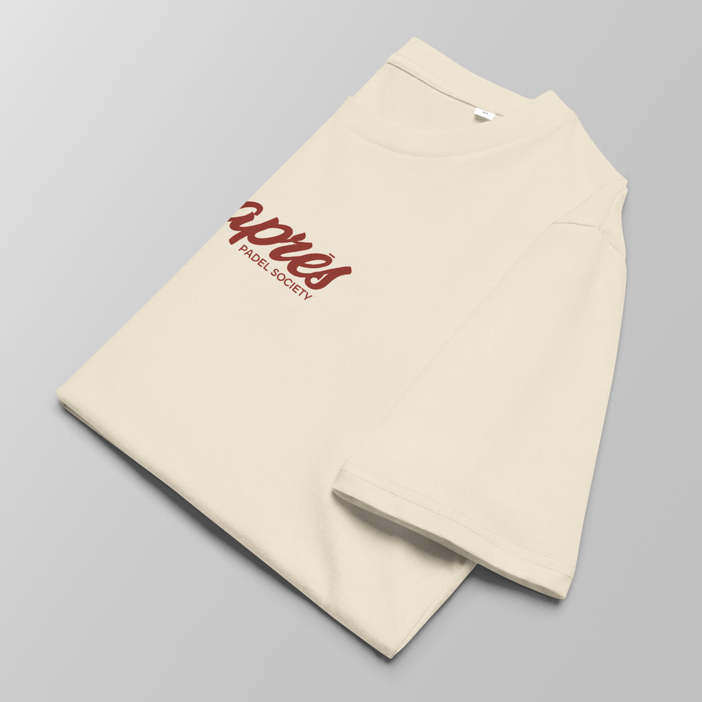 Close-up of a folded cream padel t-shirt with red 'Après Padel Society' logo centred.