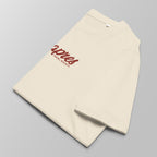 Close-up of a folded cream padel t-shirt with red 'Après Padel Society' logo centred.