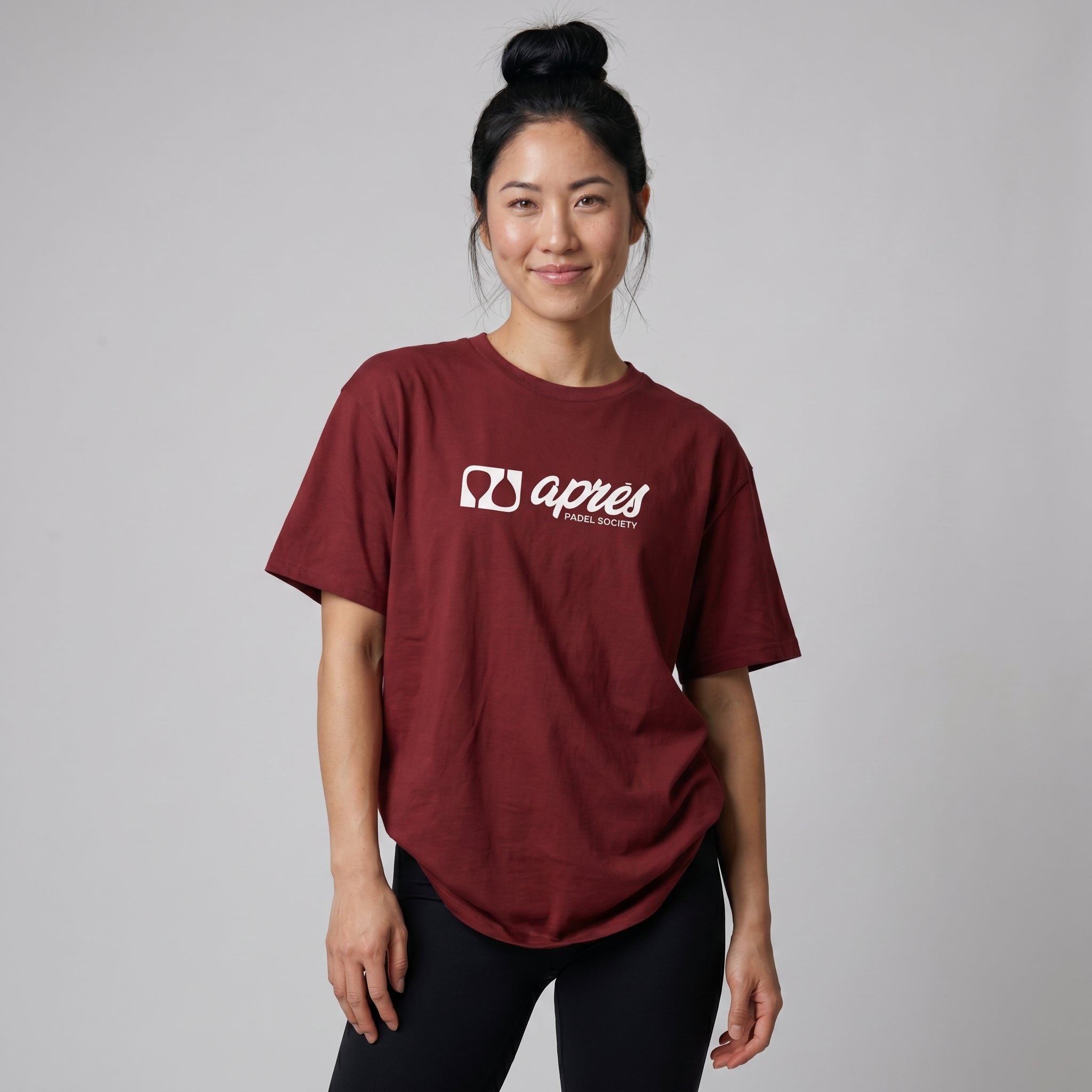 Female model wearing an oversized unisex maroon padel t-shirt in relaxed fit with a white horizontal chest logo.
