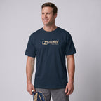 Male model wearing an oversized unisex navy blue padel t-shirt in relaxed fit with a tan horizontal chest logo.