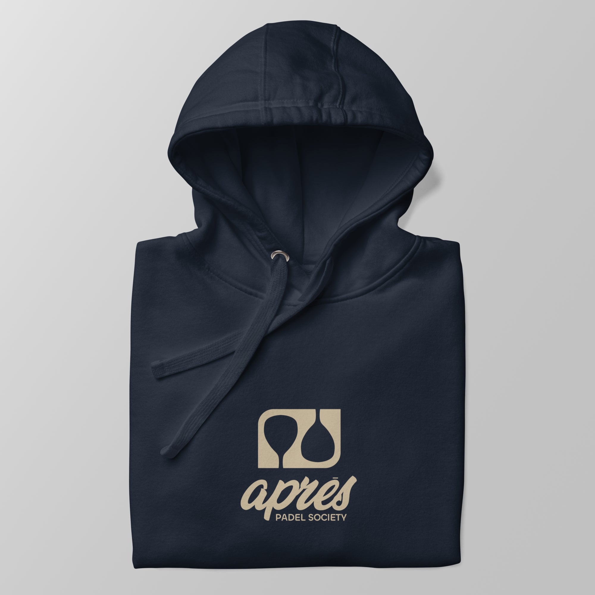 Close-up of a folded navy blue premium padel hoodie with the tan 'Après Padel Society' logo centred.