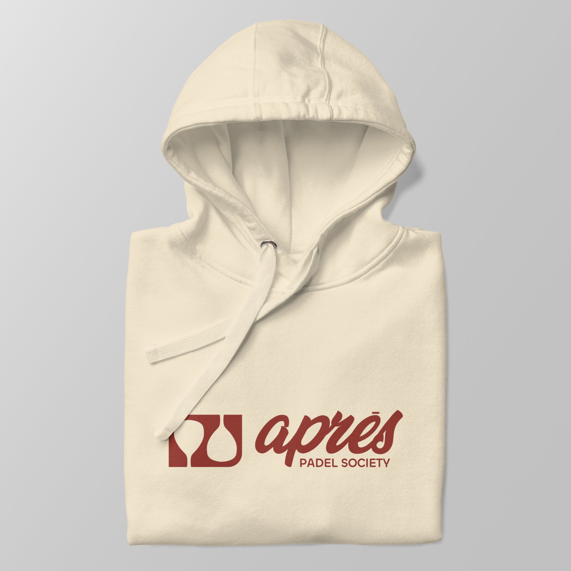 Close-up of a folded cream premium padel hoodie with the red 'Après Padel Society' logo centred.